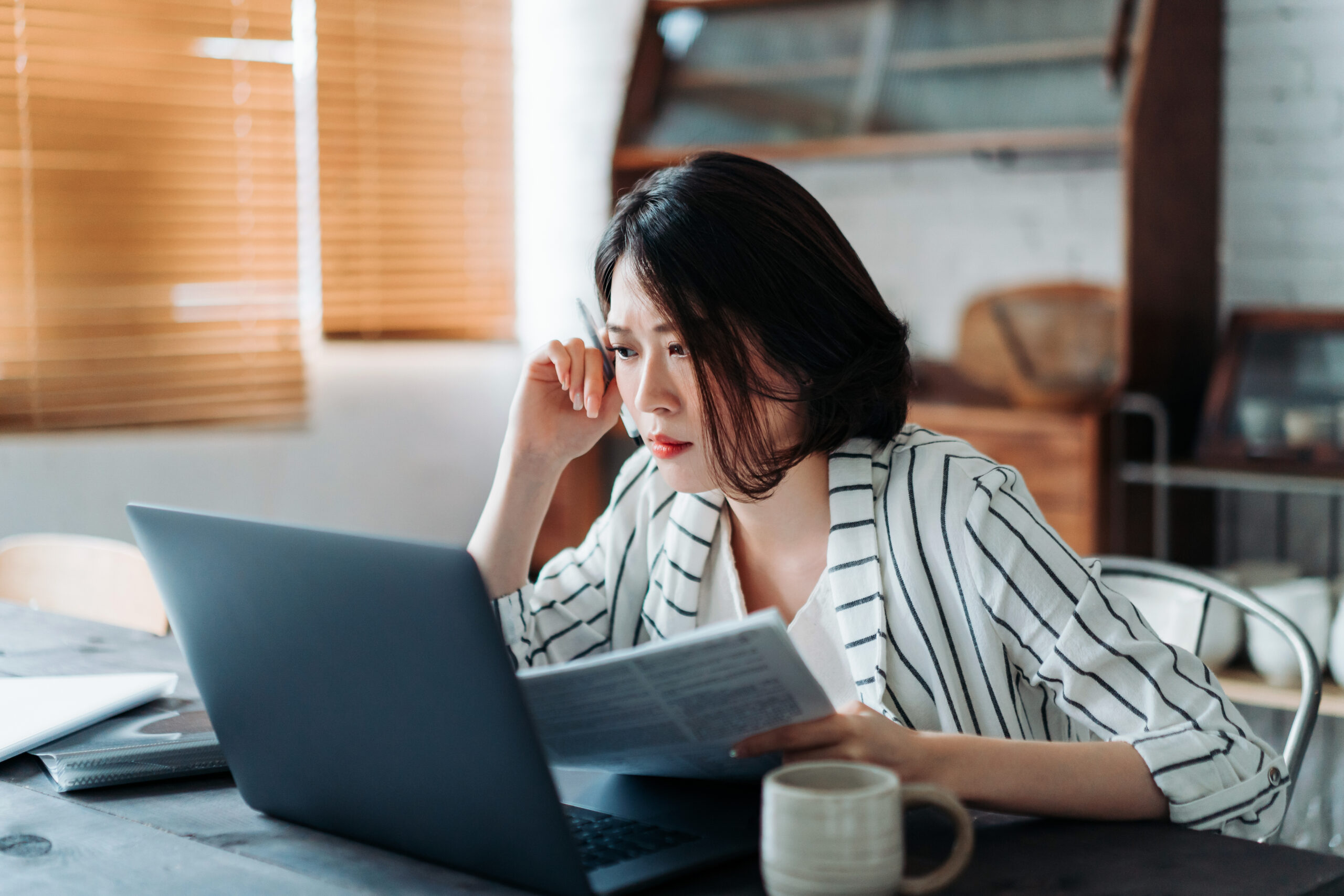 Young Asian woman handling home finances with laptop, looking worried while going through financial bills. Financial plan, tax, spending and budgets, financial problems concept